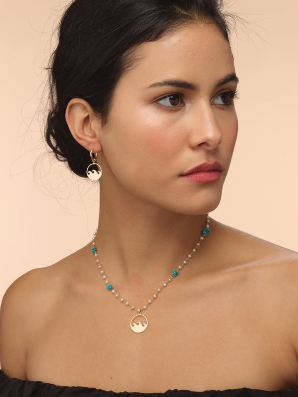 model wearing hand strung pearl necklace with gold wave talisman and blue coral.
