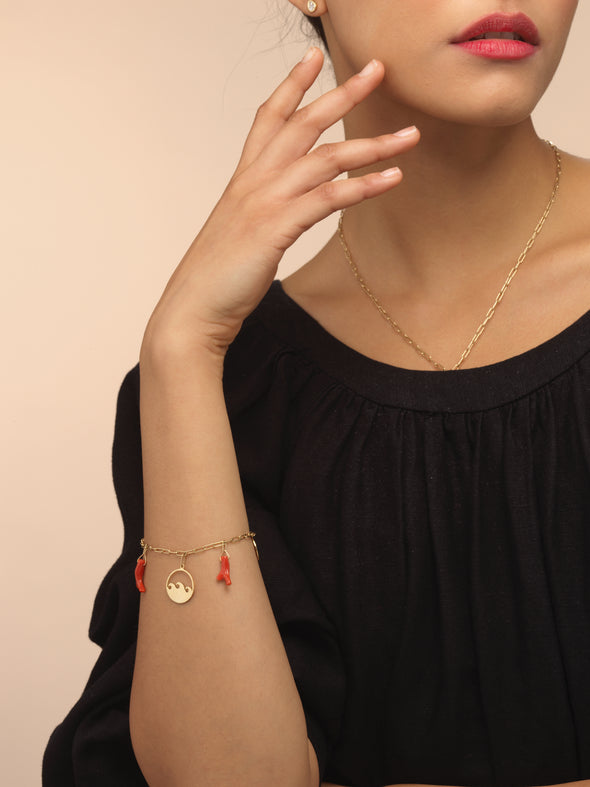 Model wearing gold charm bracelet with red coral charms.