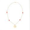 Model wearing pearl and coral necklace with gold sunburst talisman.