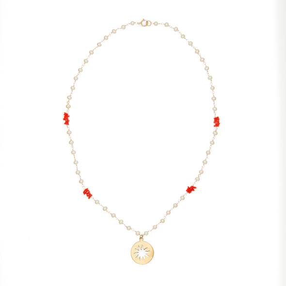 Model wearing pearl and coral necklace with gold sunburst talisman.